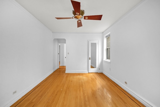 empty room with light wood-style flooring, ceiling fan, baseboards, ornamental molding, and arched walkways