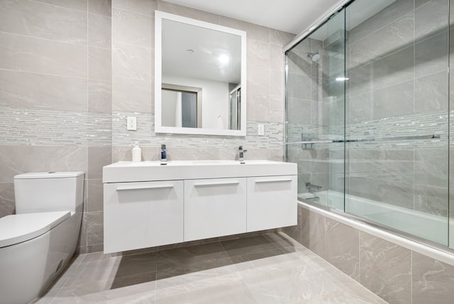 bathroom featuring toilet, tiled shower / bath combo, a sink, tile walls, and double vanity