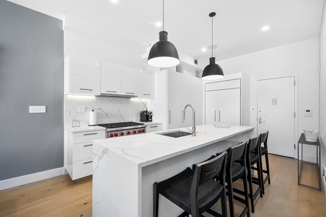 kitchen with light wood-style flooring, a sink, white cabinets, range, and backsplash