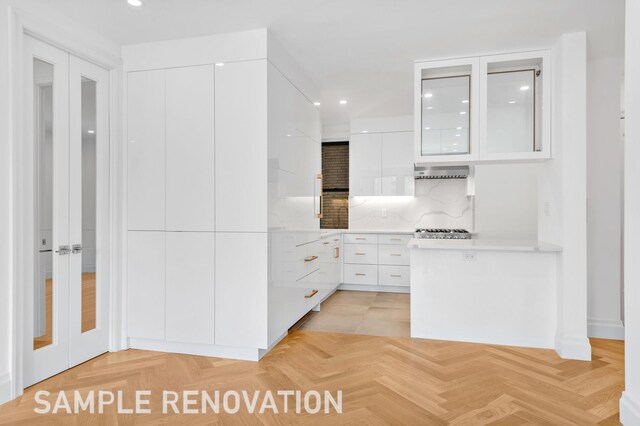 kitchen with exhaust hood, white cabinets, light countertops, modern cabinets, and glass insert cabinets