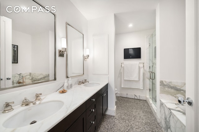 bathroom with toilet, a shower stall, double vanity, and a sink