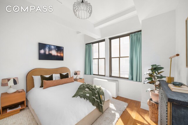 bedroom featuring beamed ceiling, wood finished floors, and baseboards