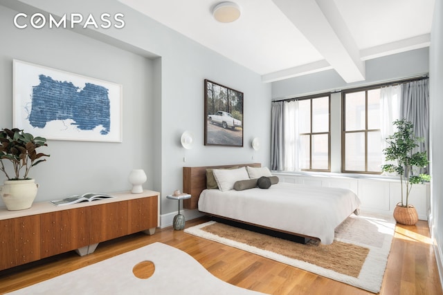 bedroom with beamed ceiling and wood finished floors