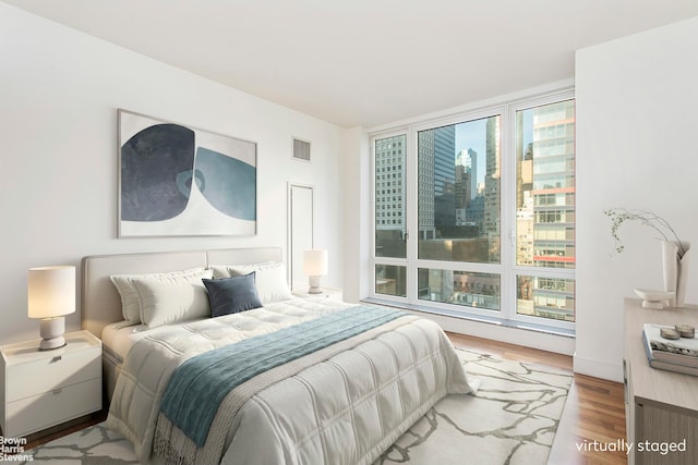 bedroom featuring wood finished floors, visible vents, and a city view