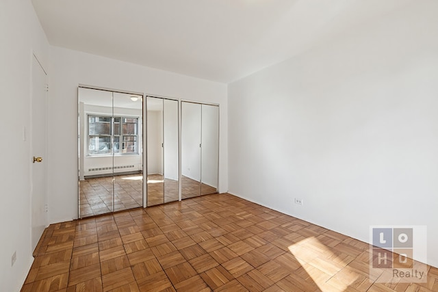 unfurnished bedroom with baseboard heating and two closets