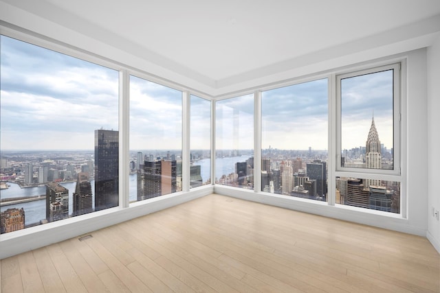 unfurnished sunroom featuring a water view, a view of city, and wood finished floors