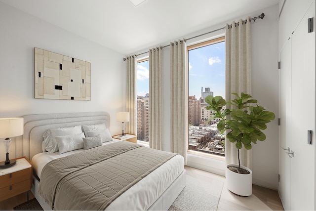 bedroom with baseboards, a city view, and light wood-style flooring