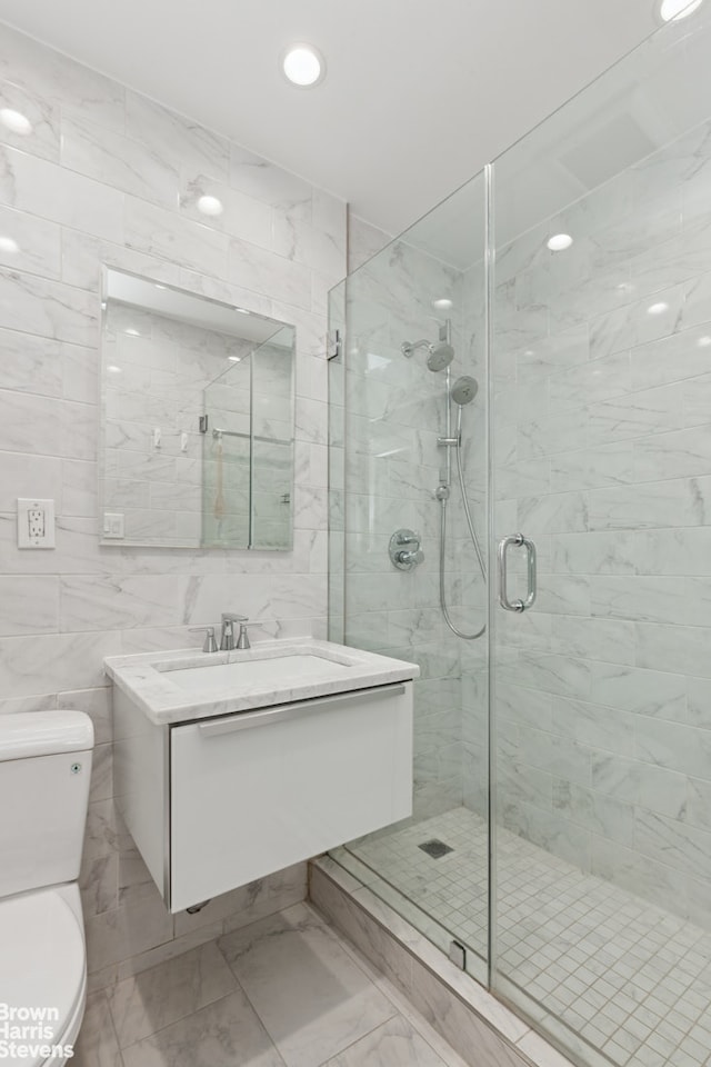 full bath with a shower stall, toilet, vanity, marble finish floor, and tile walls