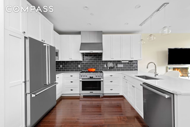 kitchen with dark wood-type flooring, a sink, backsplash, wall chimney exhaust hood, and high end appliances