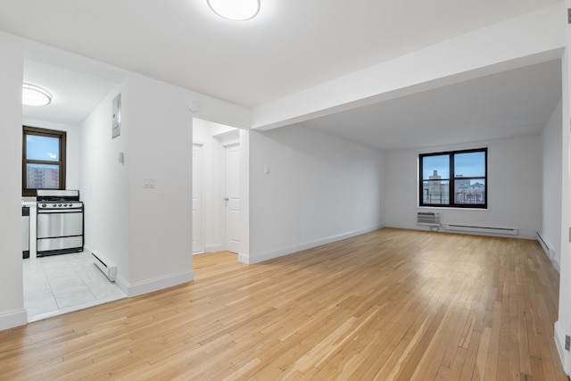 unfurnished living room featuring a baseboard heating unit, plenty of natural light, and light wood-style floors