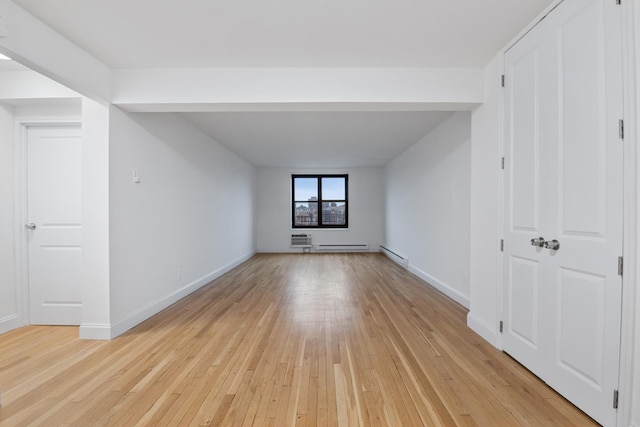 empty room with light wood-type flooring, a baseboard radiator, baseboards, and a wall mounted AC