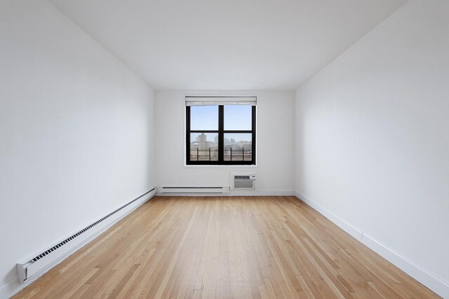 empty room featuring light wood-type flooring, a baseboard heating unit, baseboards, and an AC wall unit