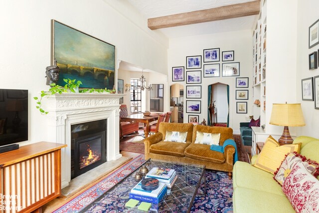 living room featuring arched walkways, beam ceiling, a glass covered fireplace, and wood finished floors