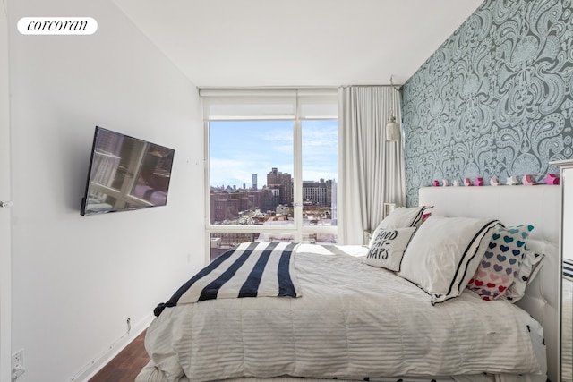 bedroom featuring a wall of windows, wood finished floors, baseboards, and wallpapered walls