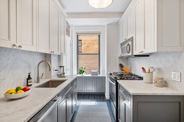 kitchen with appliances with stainless steel finishes, backsplash, a sink, and gray cabinetry