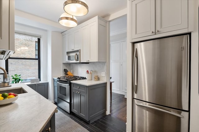 kitchen with gray cabinetry, dark wood-style flooring, a sink, appliances with stainless steel finishes, and decorative backsplash