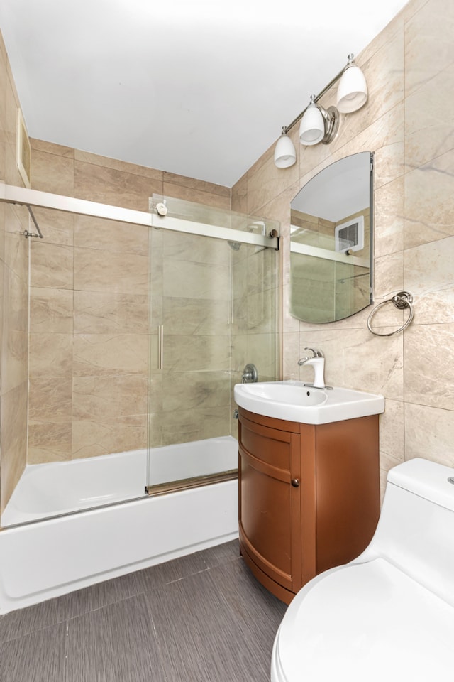 full bath with bath / shower combo with glass door, vanity, toilet, and tile walls