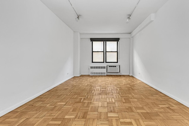 unfurnished room with an AC wall unit, radiator heating unit, rail lighting, and baseboards