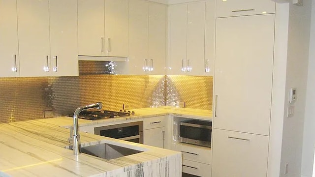 kitchen with stainless steel appliances, backsplash, white cabinets, a sink, and modern cabinets