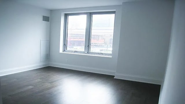 empty room with a wealth of natural light, dark wood-style flooring, visible vents, and baseboards