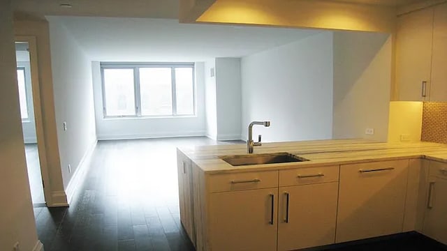 kitchen with tasteful backsplash, dark wood-type flooring, a peninsula, light countertops, and a sink