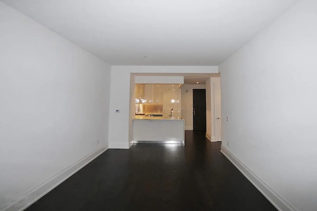 empty room featuring a sink, dark wood finished floors, and baseboards