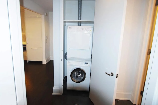 laundry room with baseboards, laundry area, dark wood-style flooring, and stacked washer / drying machine