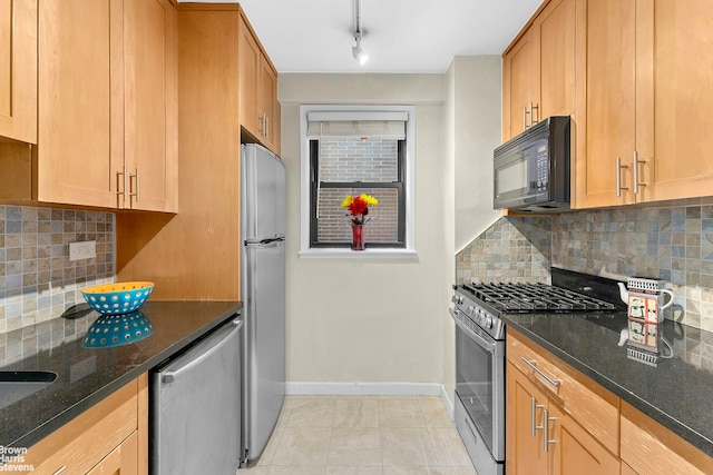 kitchen featuring baseboards, backsplash, stainless steel appliances, and dark stone counters