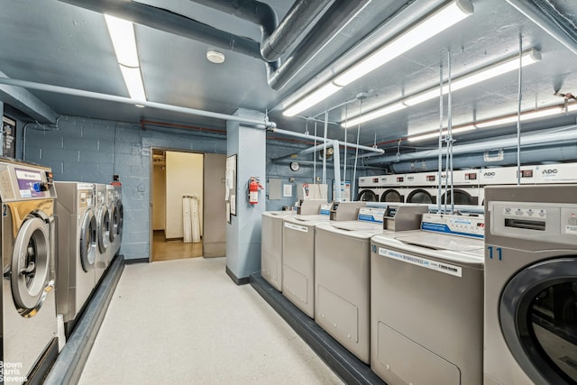 community laundry room with concrete block wall, separate washer and dryer, and light floors