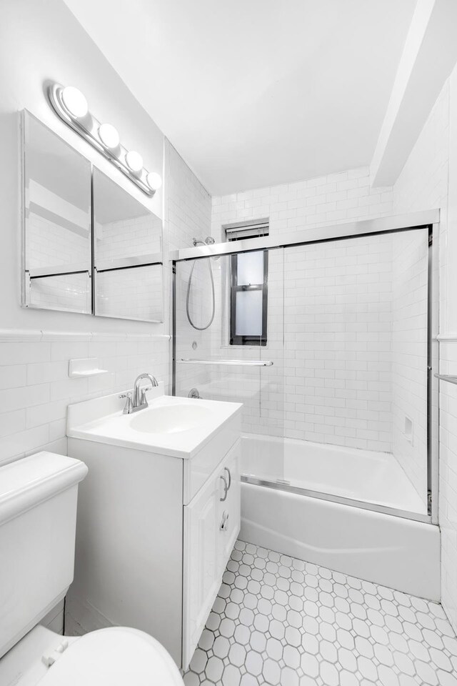 bathroom featuring tile walls, enclosed tub / shower combo, vanity, and toilet