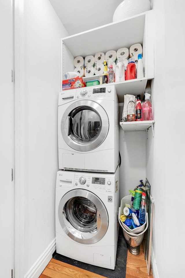 laundry area featuring baseboards, laundry area, stacked washer / dryer, and wood finished floors