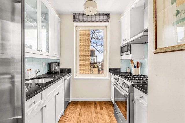 kitchen featuring stainless steel appliances, a sink, light wood-type flooring, white cabinets, and tasteful backsplash