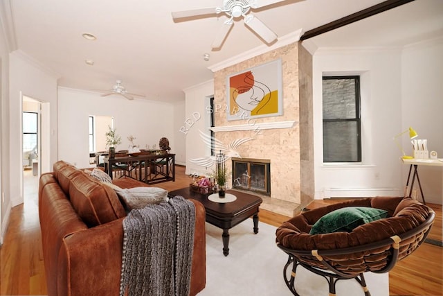 living room with a premium fireplace, crown molding, a ceiling fan, and wood finished floors