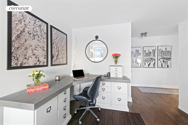 office space featuring dark wood-type flooring, built in desk, and baseboards