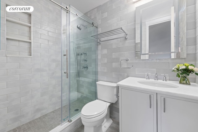 full bathroom with vanity, a stall shower, toilet, and tile walls