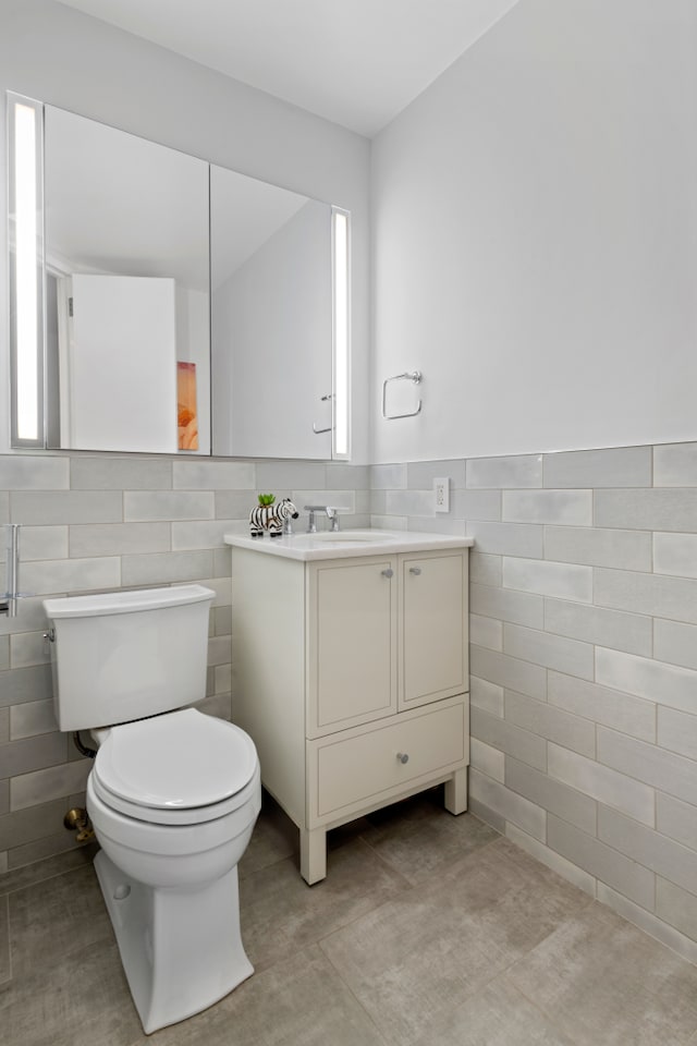 bathroom with toilet, wainscoting, tile walls, and vanity