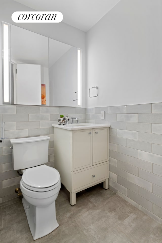 bathroom featuring wainscoting, tile walls, toilet, and vanity