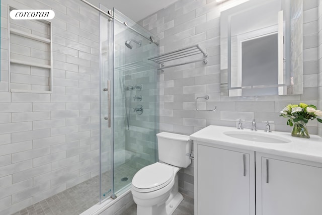 bathroom featuring tasteful backsplash, toilet, vanity, a shower stall, and tile walls