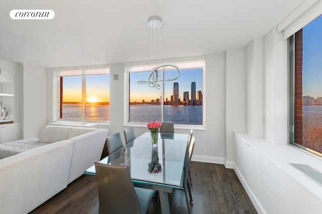 dining area with an inviting chandelier, a water view, dark wood-style floors, and visible vents