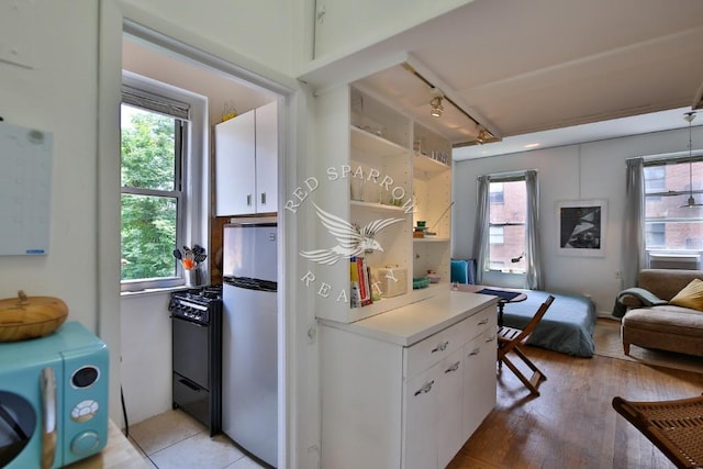 kitchen featuring freestanding refrigerator, gas range oven, plenty of natural light, and white cabinets