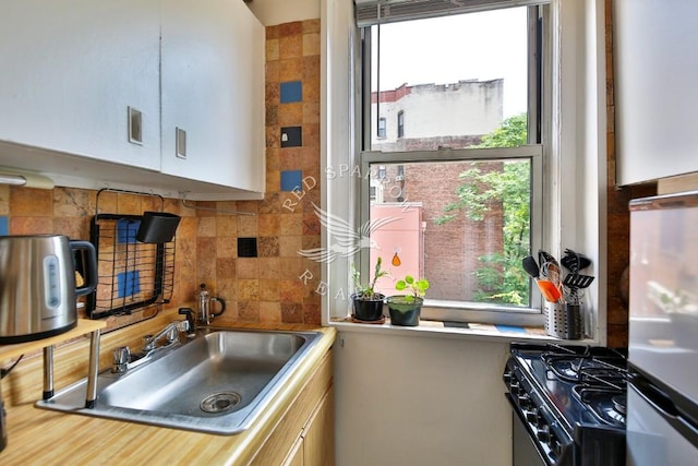 kitchen featuring light countertops, tasteful backsplash, black range with gas stovetop, and a sink