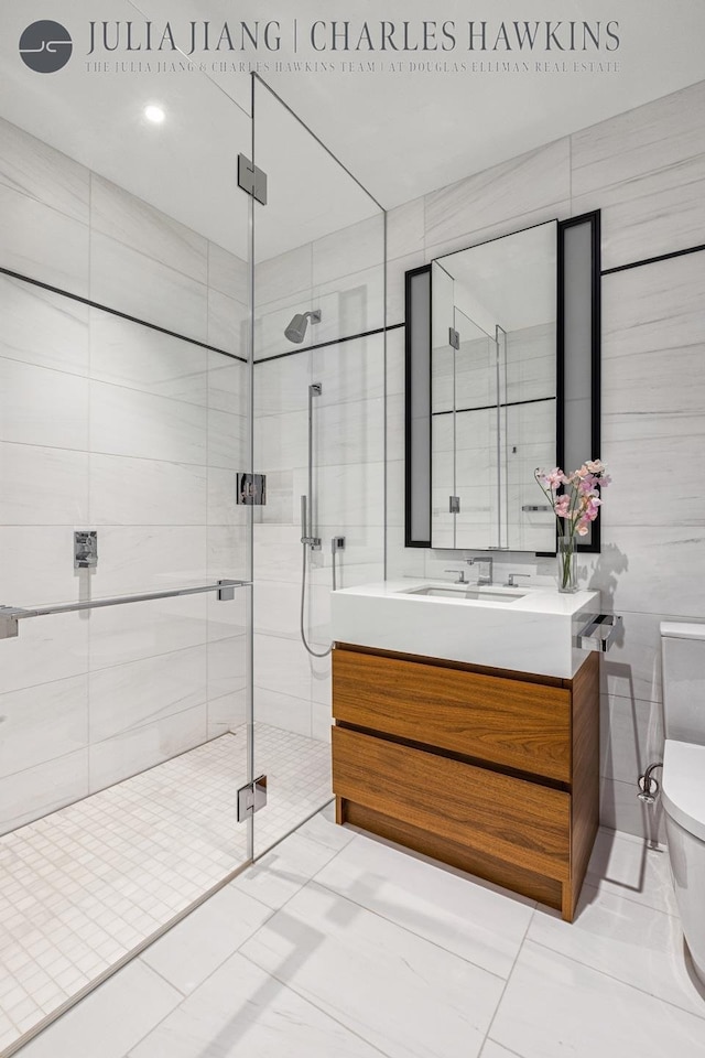 bathroom with tile walls, toilet, a stall shower, vanity, and tile patterned flooring