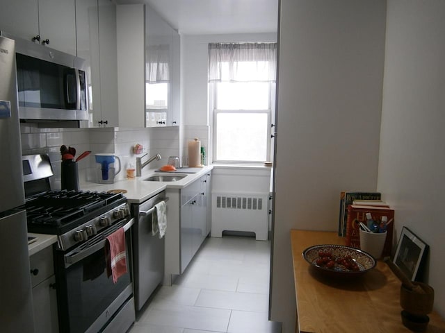 kitchen with decorative backsplash, radiator, appliances with stainless steel finishes, light countertops, and a sink