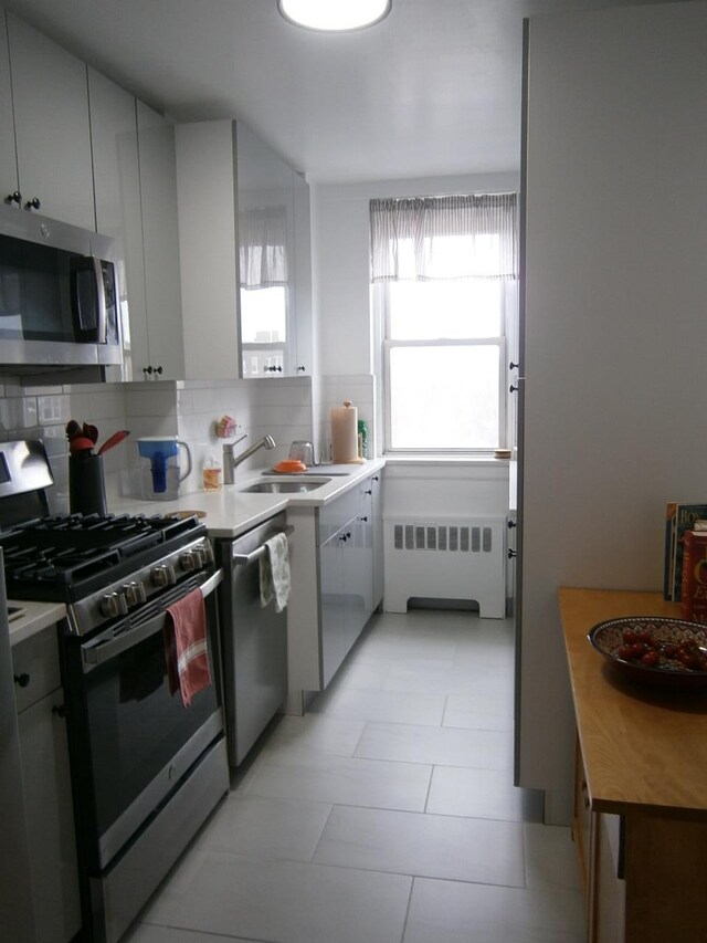 kitchen featuring stainless steel appliances, light countertops, decorative backsplash, radiator heating unit, and a sink