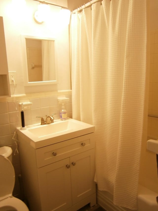 full bathroom featuring toilet, vanity, tile walls, wainscoting, and shower / bath combination with curtain