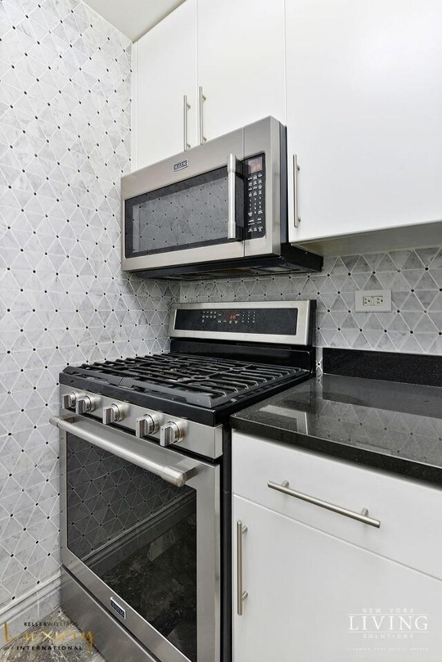 kitchen featuring appliances with stainless steel finishes, white cabinets, dark stone countertops, and tasteful backsplash