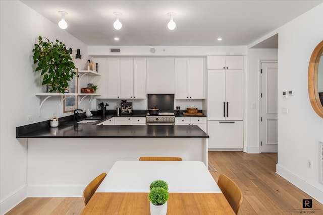 kitchen featuring visible vents, dark countertops, a peninsula, open shelves, and a sink