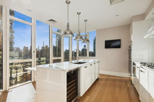 kitchen featuring visible vents, a sink, wood finished floors, a wall of windows, and beverage cooler