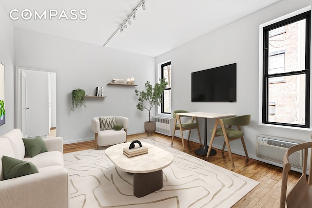 living area with wood-type flooring, rail lighting, an AC wall unit, and baseboards