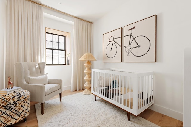 bedroom with baseboards, a nursery area, and wood finished floors